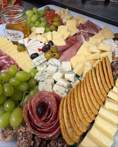 Platter of assorted meats, cheeses, and crackers with a jar of jam on a kitchen counter.